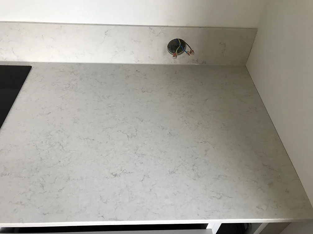 Polerad bänkskiva i Silestone Snowy Ibiza med uppvikt stänkkant och urtag för eluttag intill induktionshällen i ett kök i Lund.