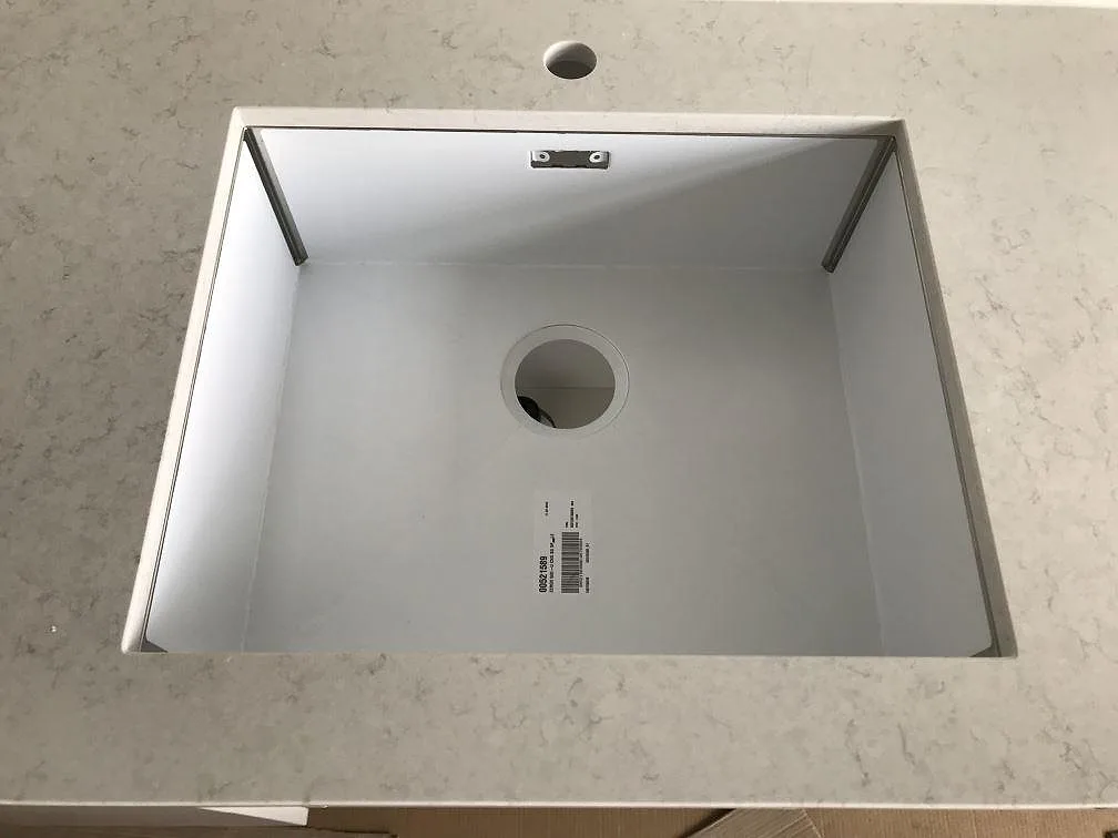 Närbild på den underlimmade rostfria diskhon i köksbänkskivan av polerad Silestone Snowy Ibiza i ett kök i Lund.