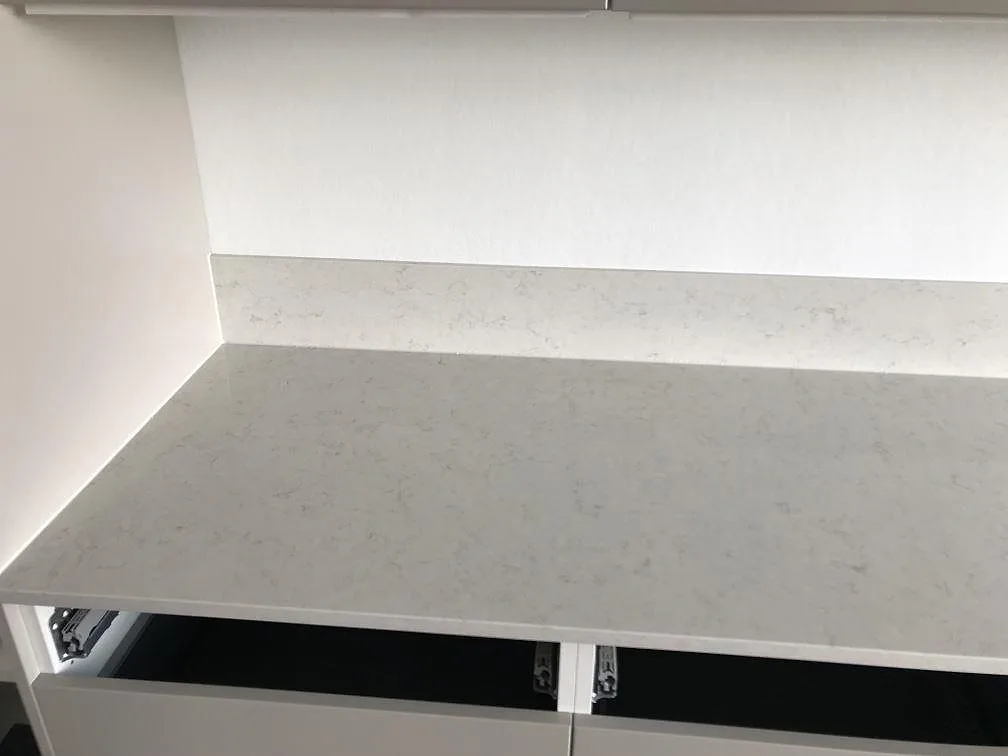 Polerad köksbänkskiva i Silestone Snowy Ibiza med låg uppvikt stänkkant i samma sten mot vit vägg i ett kök i Lund.