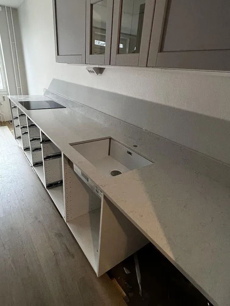 Köksbänkskiva i Silestone Snowy Ibiza med underlimmad diskho och uppvikt stänkskydd över öppna köksstommar i Lund.