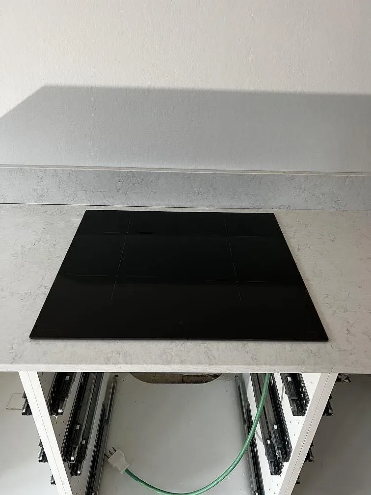 Svart induktionshäll nedsänkt i en vit Silestone Snowy Ibiza-bänkskiva med ett stänkskydd i samma polerade komposit i ett kök i Lund.