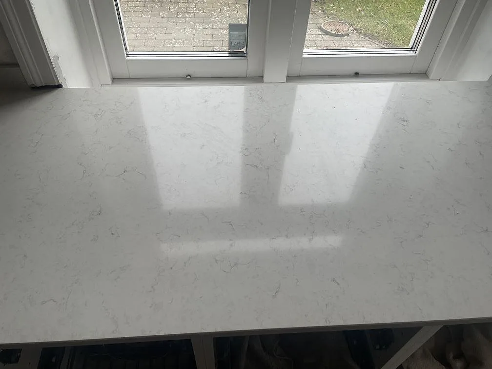 Polerad köksbänkskiva i vit Silestone Snowy Ibiza under ett fönster i ett kök i Lund, med spegelblank yta och diskret ådring.