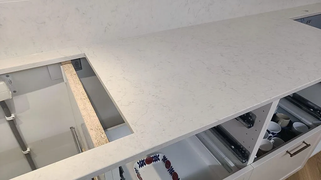Lång bänkyta i vit Silestone Snowy Ibiza, polerad kvartskomposit, med hällöppning över vita köksstommar i Lund.