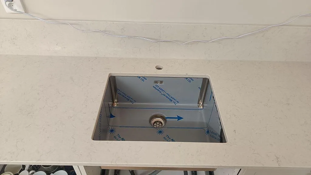 Detalj av rostfri diskho monterad under en polerad Silestone Snowy Ibiza bänkskiva med stänkskydd i Lund.