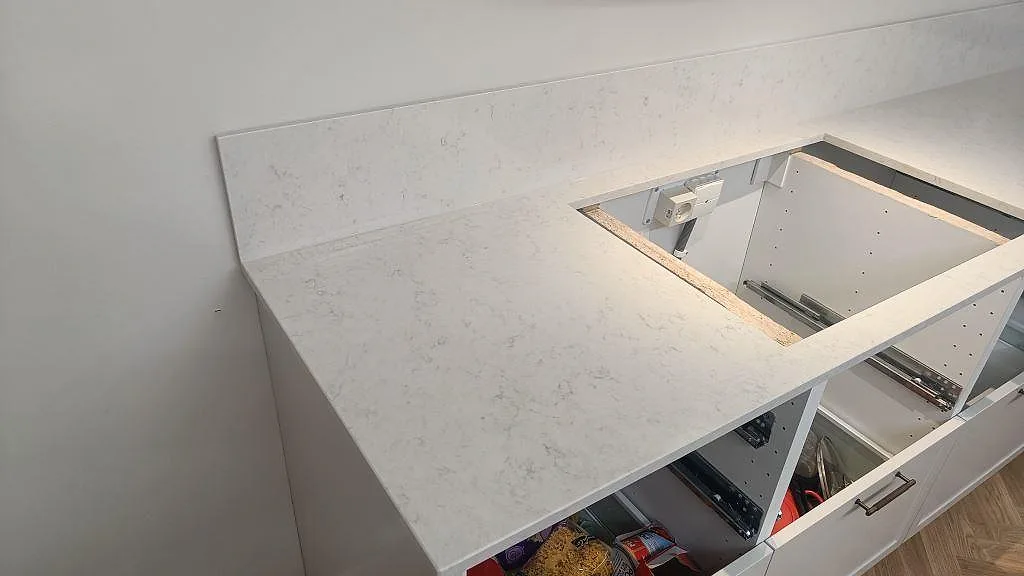 Köksbänkskiva i vit Silestone Snowy Ibiza, polerad, med uppvikt stänkskydd och hällöppning i ett kök i Lund.