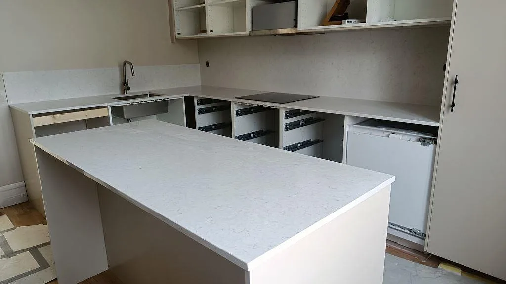 Köksbänkskiva i polerad Silestone Snowy Ibiza med köksö, bänkrad och stänkskydd i ett kök under montering i Lund.