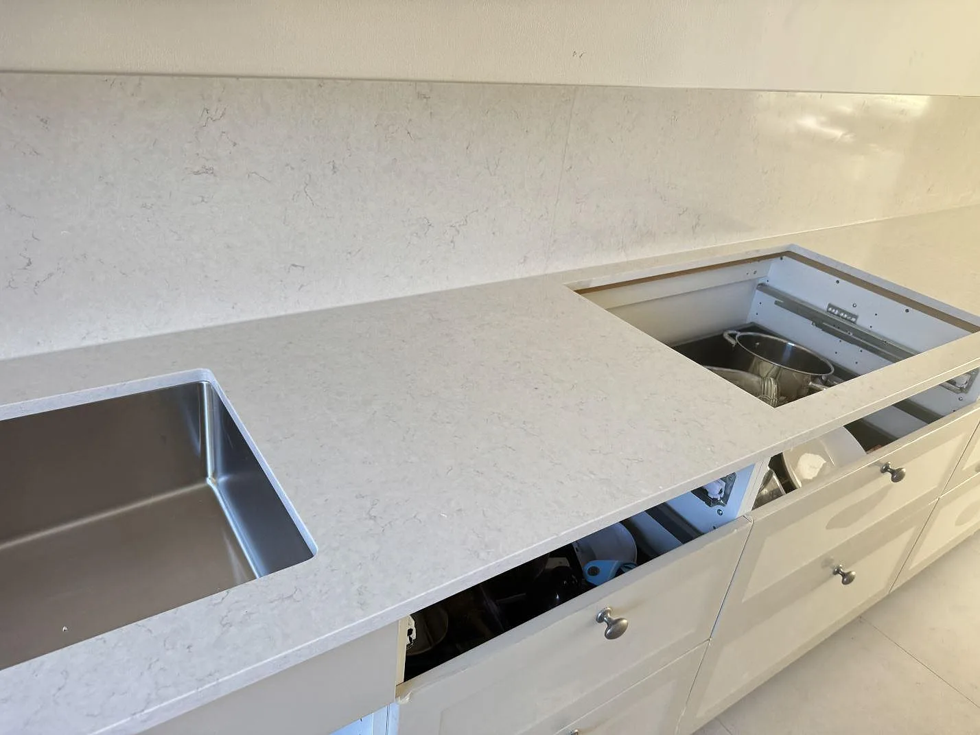 Lång arbetsyta i polerad Silestone Snowy Ibiza med diskzon, öppning i bänkskivan och stänkskydd i Lund.
