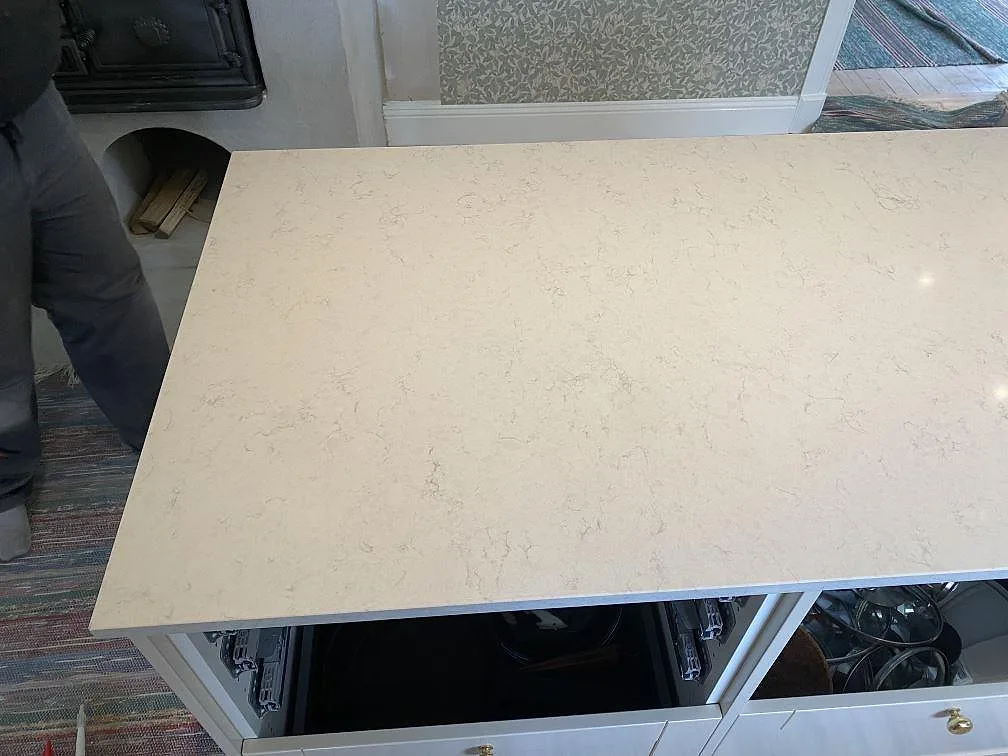 Köksö i polerad Silestone Snowy Ibiza med ljus ådring och öppna skåpstommar under montering i Målsryd.