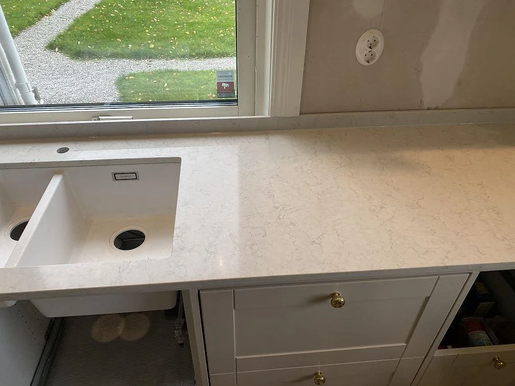 Närbild på köksbänkskiva i polerad Silestone Snowy Ibiza med vit ho, fönsterläge och öppen stomme i Målsryd.