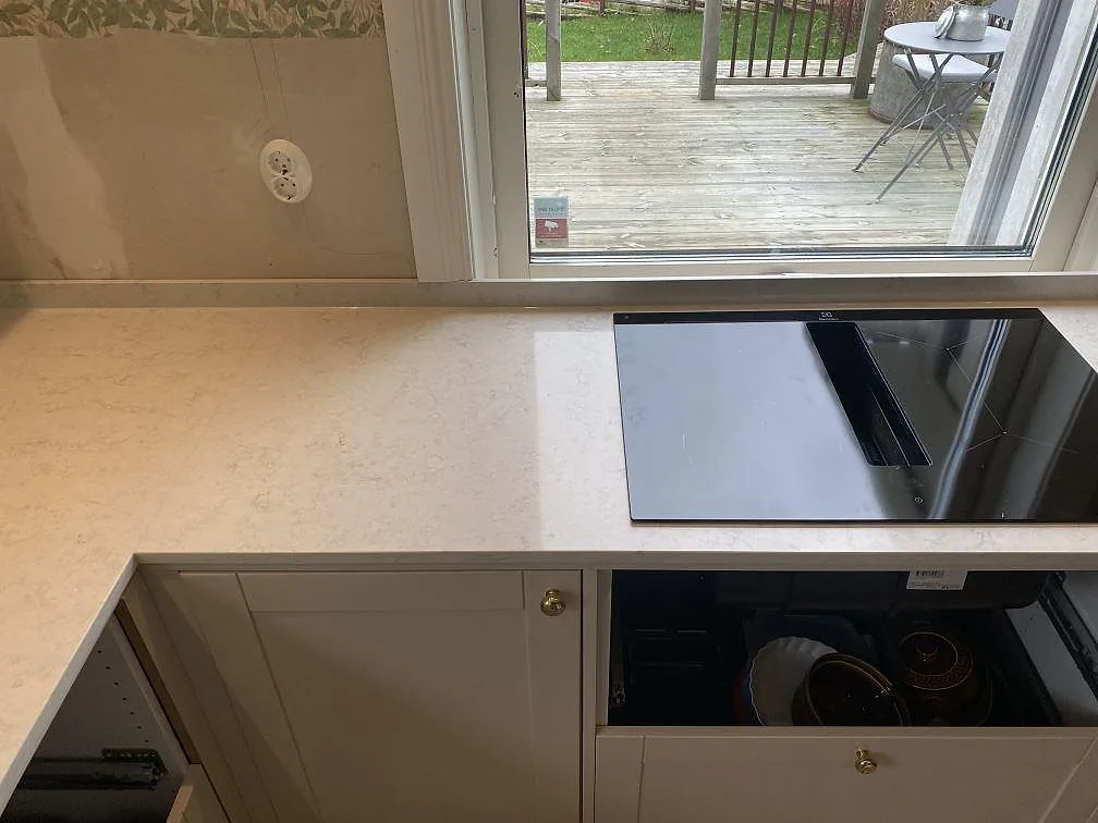 Köksbänkskiva i polerad Silestone Snowy Ibiza med svart häll och uppvikt stänkkant vid fönster i Målsryd.