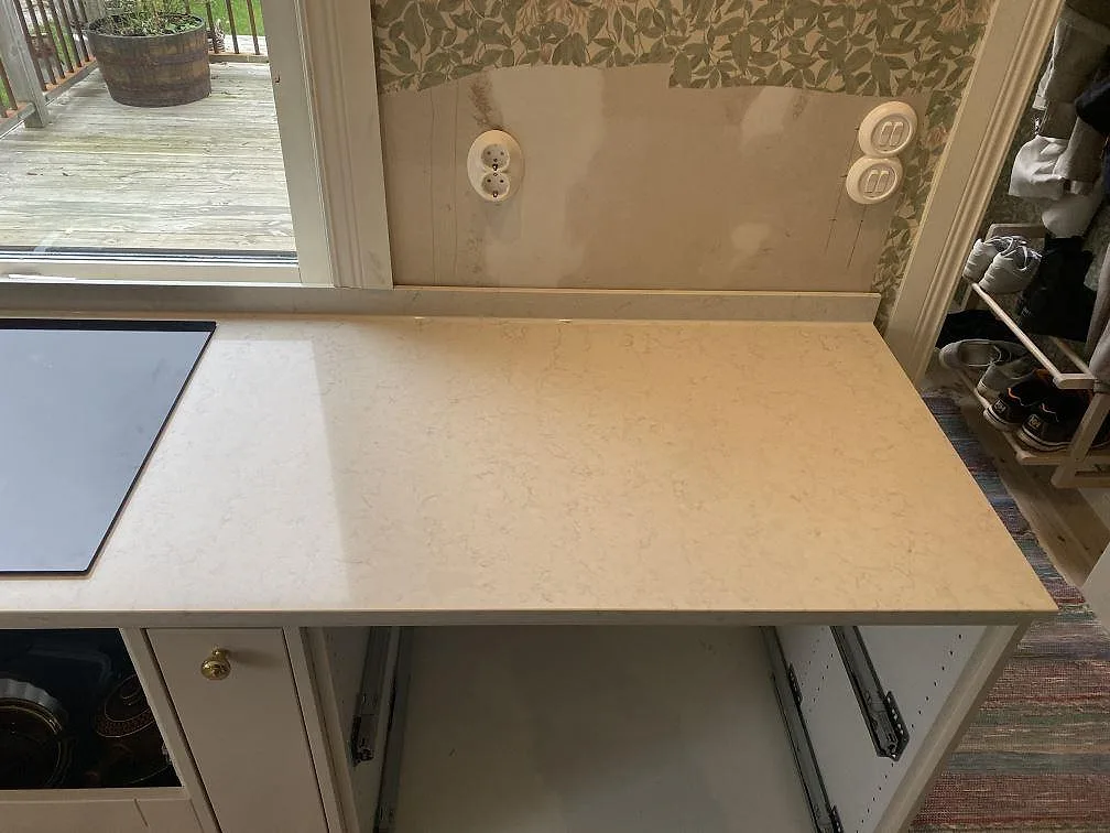Hällsektion i polerad Silestone Snowy Ibiza med ljus komposityta, lågt stänkskydd och grågröna skåp i Målsryd.