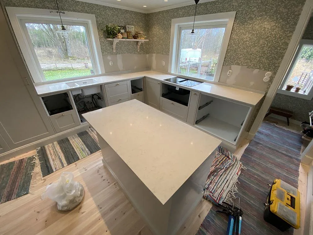 Köksbänkskiva och köksö i polerad Silestone Snowy Ibiza med ljus ådring i ett kök under montering i Målsryd.
