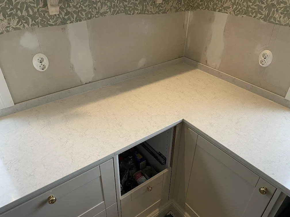 Hörndel av köksbänkskiva i polerad Silestone Snowy Ibiza med låg stänkkant och öppna skåpstommar i Målsryd.