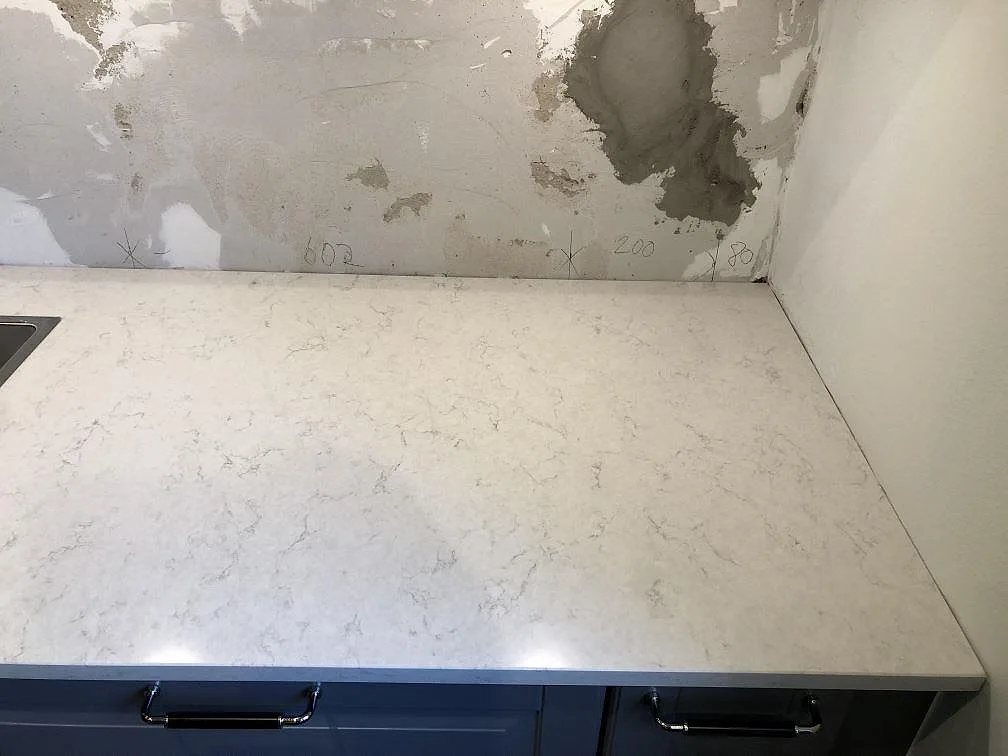 Polerad bänkskiva i Silestone Snowy Ibiza med mjuk grå ådring över en lång köksbänk i Malmö, monterad på marinblå underskåp med krombygelhandtag.