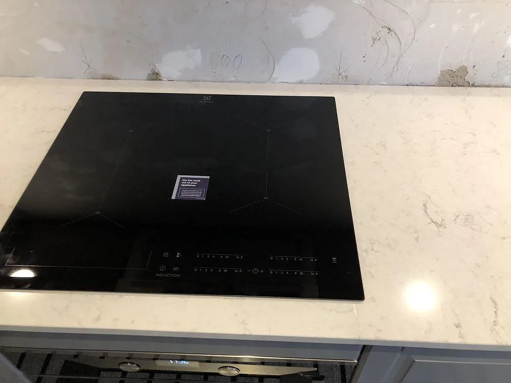 Svart induktionshäll planmonterad i en polerad Silestone Snowy Ibiza köksbänkskiva i Malmö, sedd ovanifrån.