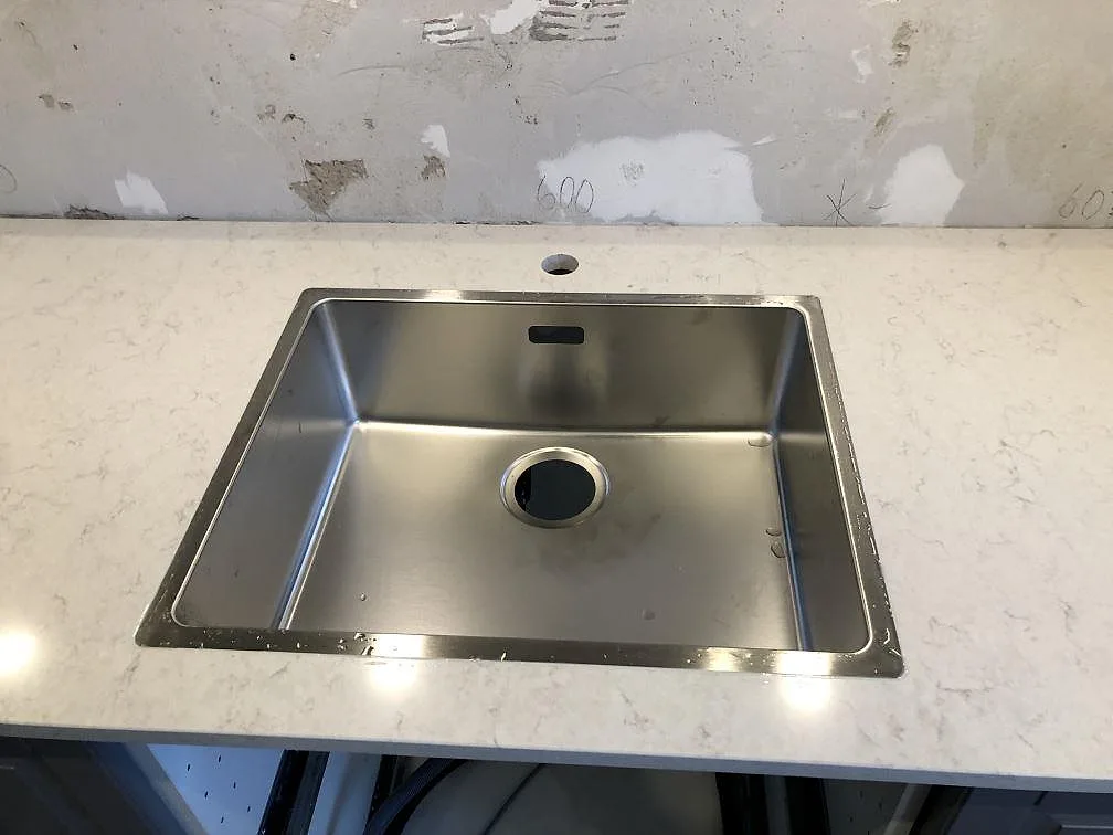 Borstad rostfri diskho monterad i nivå med en vit Silestone Snowy Ibiza köksbänkskiva i polerad finish i ett kök i Malmö.