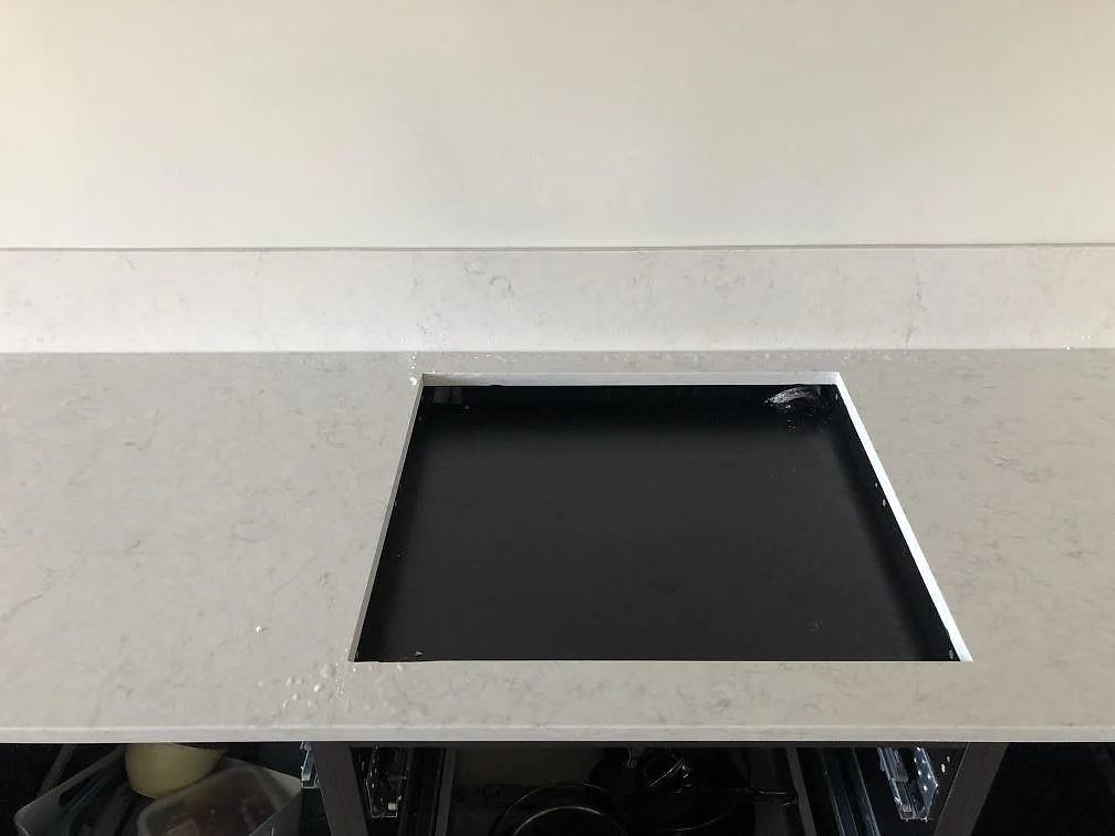 Hörndetalj av en vit Silestone Snowy Ibiza-bänkskiva med blandarhål och uppvikt stänkkant mot mörka köksstommar i Malmö.