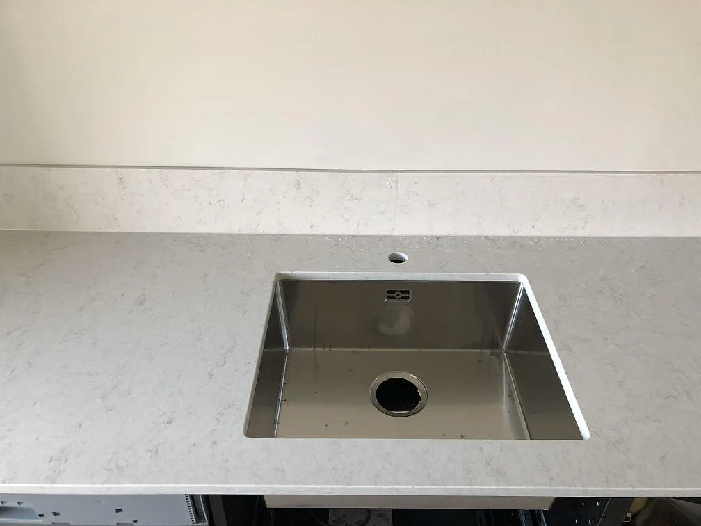 Vit Silestone Snowy Ibiza-bänkskiva med fyrkantig urtagning för infälld induktionshäll och uppvikt stänkkant i ett kök i Malmö.