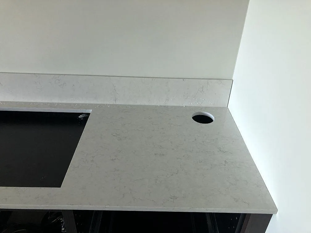Vit Silestone Snowy Ibiza-bänkskiva i kvartskomposit med infälld induktionshäll i svart glas och stänkkant i ett kök i Malmö.