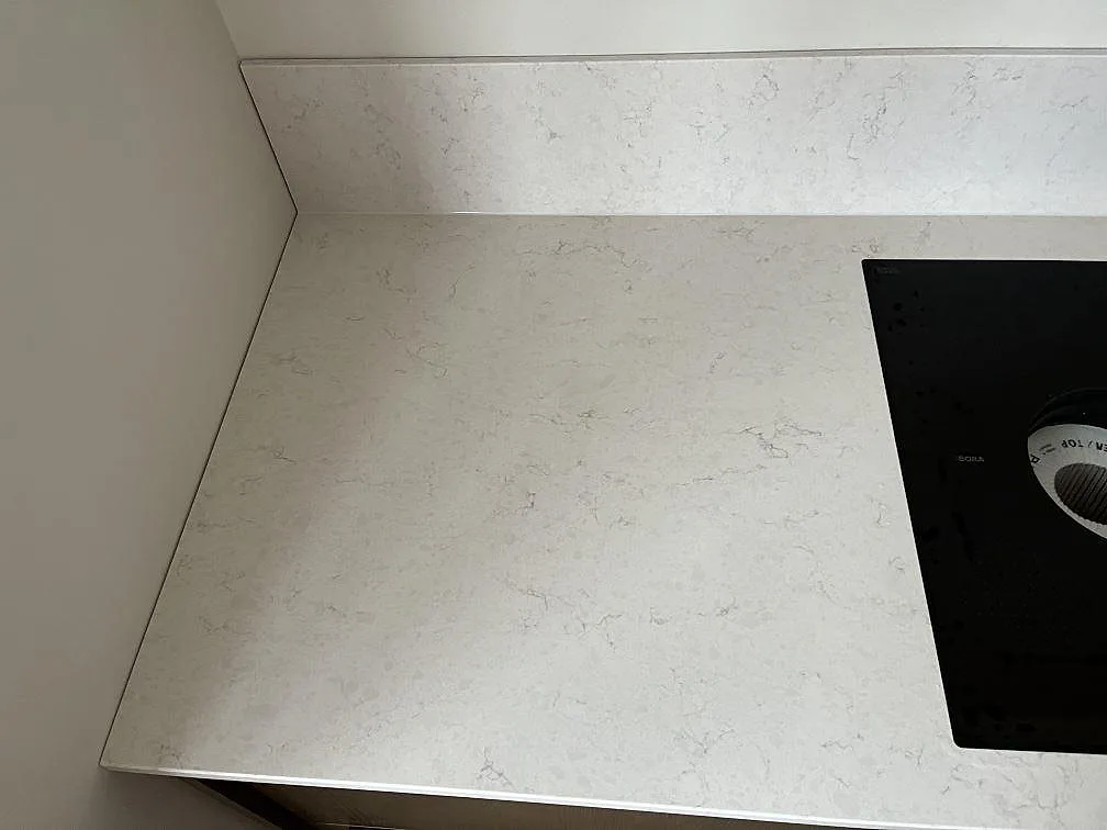 Närbild på den vita ådringen i en Silestone Snowy Ibiza-bänkskiva med induktionshäll och uppvikt stänkkant i ett kök i Malmö.