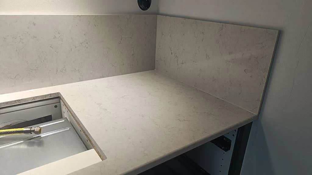 Hörn med köksbänkskiva och uppvikt stänkskydd i ljus Silestone Snowy Ibiza, polerad komposit, i ett kök i Malmö.