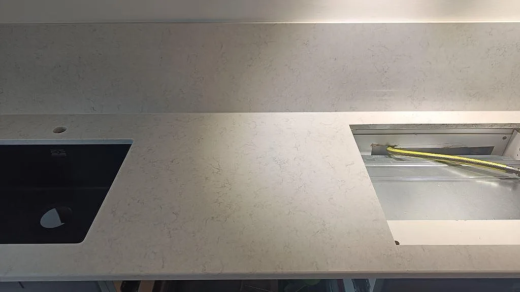 Bänkskiva i Silestone Snowy Ibiza med svart underlimmad kompositdiskho och separat kranhål samt uttag för häll i ett kök i Malmö.