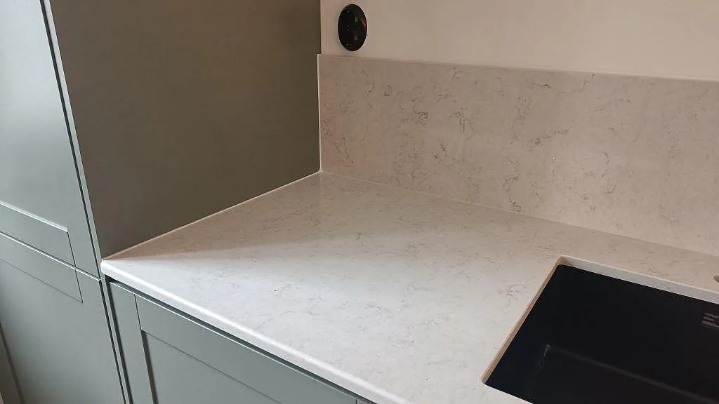 Bänkskiva och stänkskydd i ljus Silestone Snowy Ibiza med svart underlimmad diskho i hörnet av ett kök i Malmö.