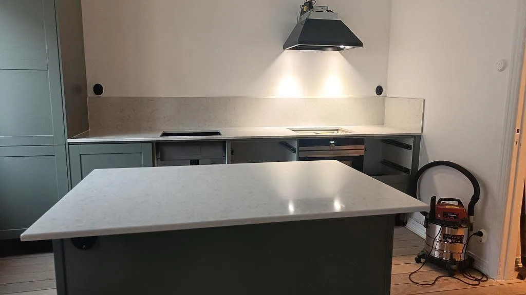 Köksbänkskiva och köksö i ljus Silestone Snowy Ibiza, polerad kvartskomposit, med uppvikt stänkskydd i ett kök under montering i Malmö.