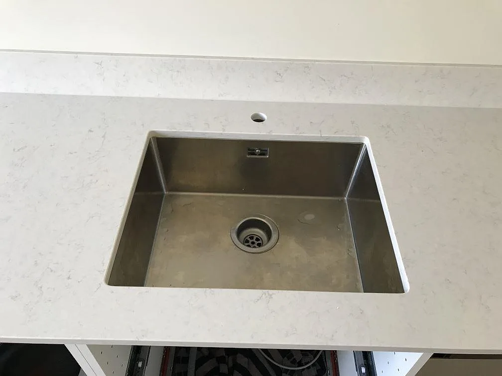 Närbild på en underlimmad rostfri diskho i en köksbänkskiva i vit Silestone Snowy Ibiza, polerad, i Malmö.
