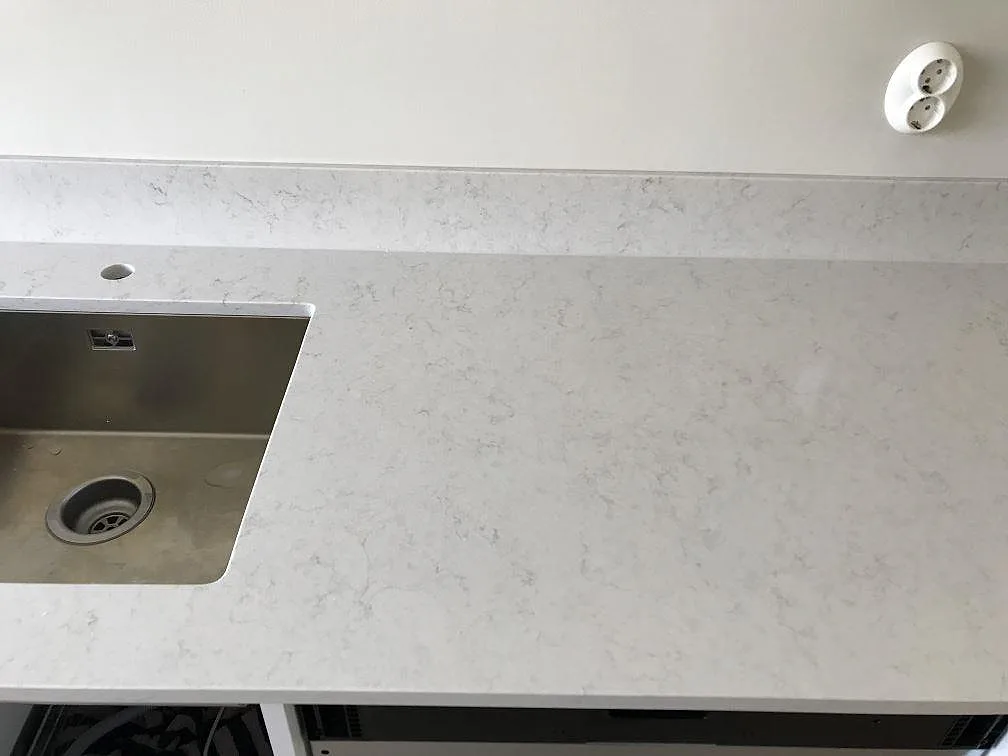 Köksbänkskiva i Silestone Snowy Ibiza, polerad komposit, med underlimmad rostfri diskho och separat borrat blandarhål i stenen i ett kök i Malmö.