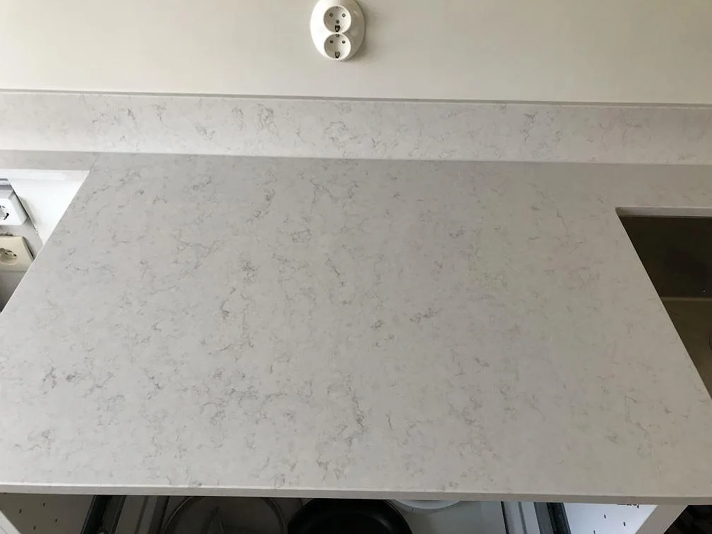 Köksbänkskiva i polerad Silestone Snowy Ibiza med fin grå ådring och uppvikt stänkkant i ett kök i Malmö.