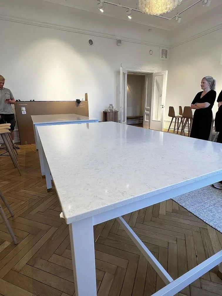 Närbild på polerad bordsskiva i Silestone Snowy Ibiza med vit kant och bordsben i ett rum med fiskbensparkett i Malmö.