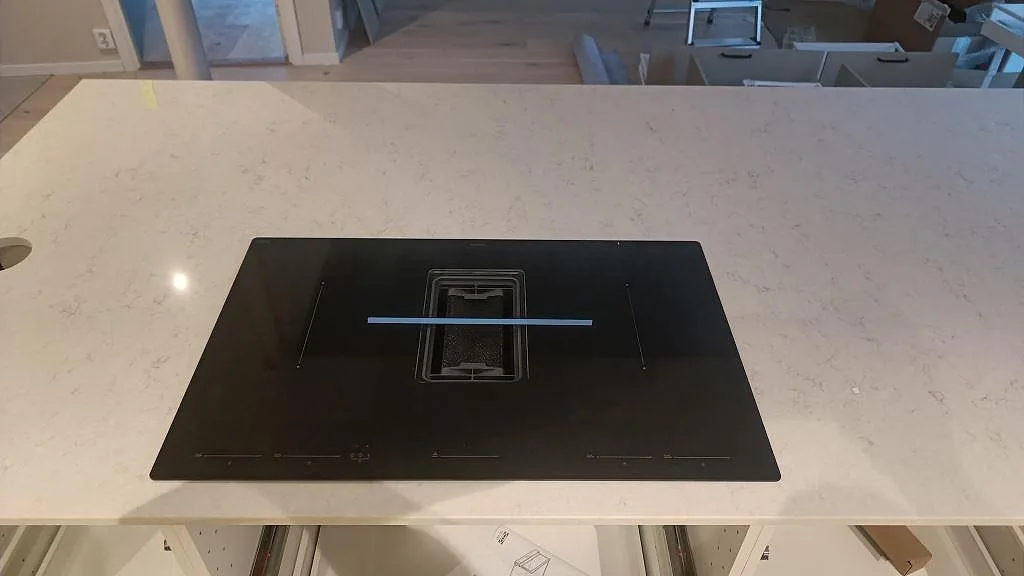 Närbild på polerad Silestone Snowy Ibiza bänkskiva med nedsänkt induktionshäll och håltagning för blandare i ett kök i Malmö.