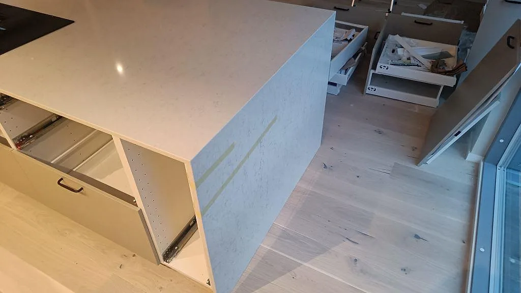 Köksö i polerad Silestone Snowy Ibiza med nedvikt gavel och öppna lådor under pågående montering i Malmö.