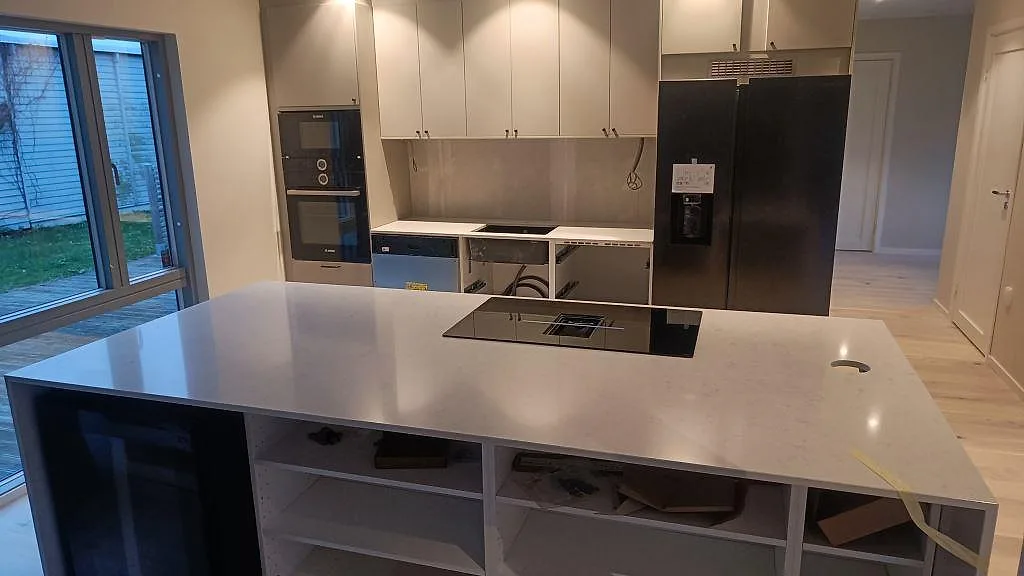 Köksbänkskiva och köksö i vit Silestone Snowy Ibiza, polerad, med nedsänkt induktionshäll i ett kök under montering i Malmö.