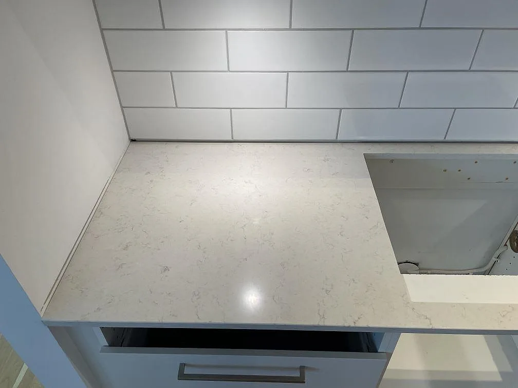 Polerad köksbänkskiva i Silestone Snowy Ibiza mot vitt metrokakel och blågrå köksluckor i ett kök i Malmö.