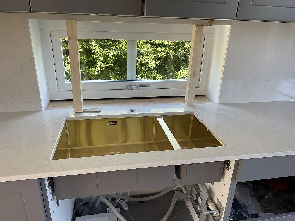 Köksbänkskiva i polerad Silestone Snowy Ibiza komposit med mässingsfärgad underlimmad dubbelho vid fönster i Malmö.