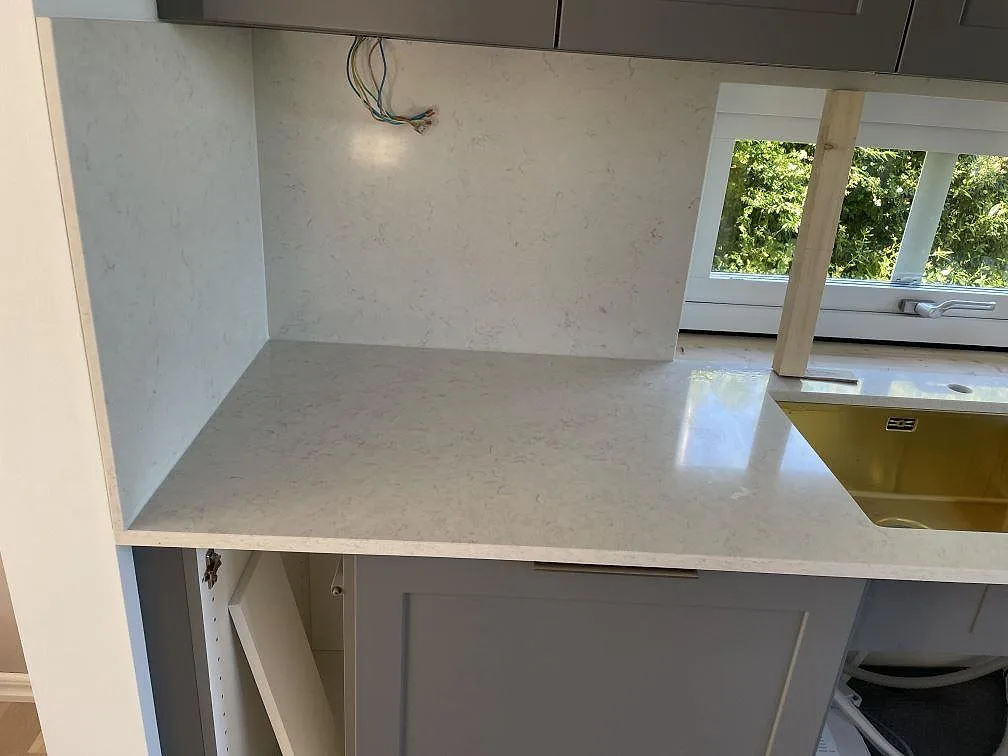 Köksbänkskiva och väggyta i polerad Silestone Snowy Ibiza komposit intill dubbelho i Malmö.