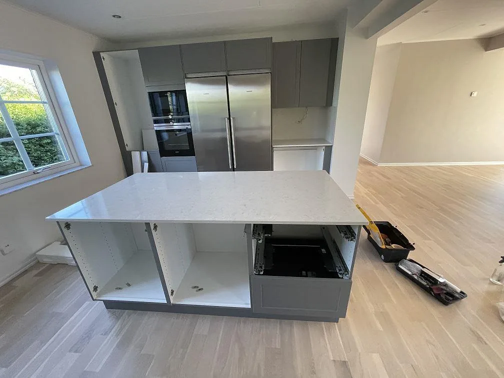 Polerad köksö i Silestone Snowy Ibiza komposit framför grå skåp och vitvaror i ett kök i Malmö.