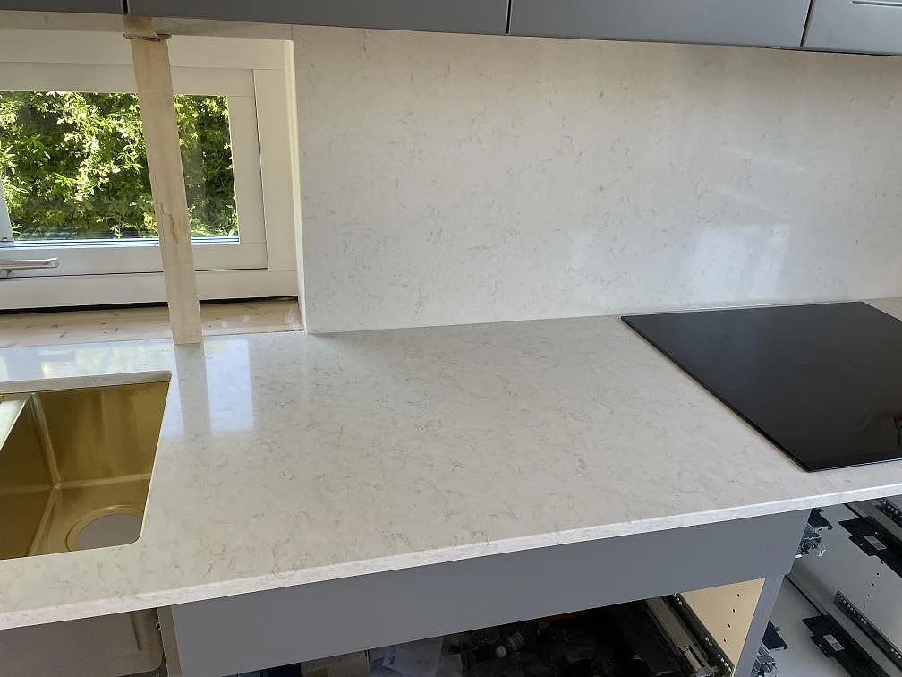 Polerad Silestone Snowy Ibiza komposit med svart häll, mässingsfärgad ho och stänkskydd i kök i Malmö.