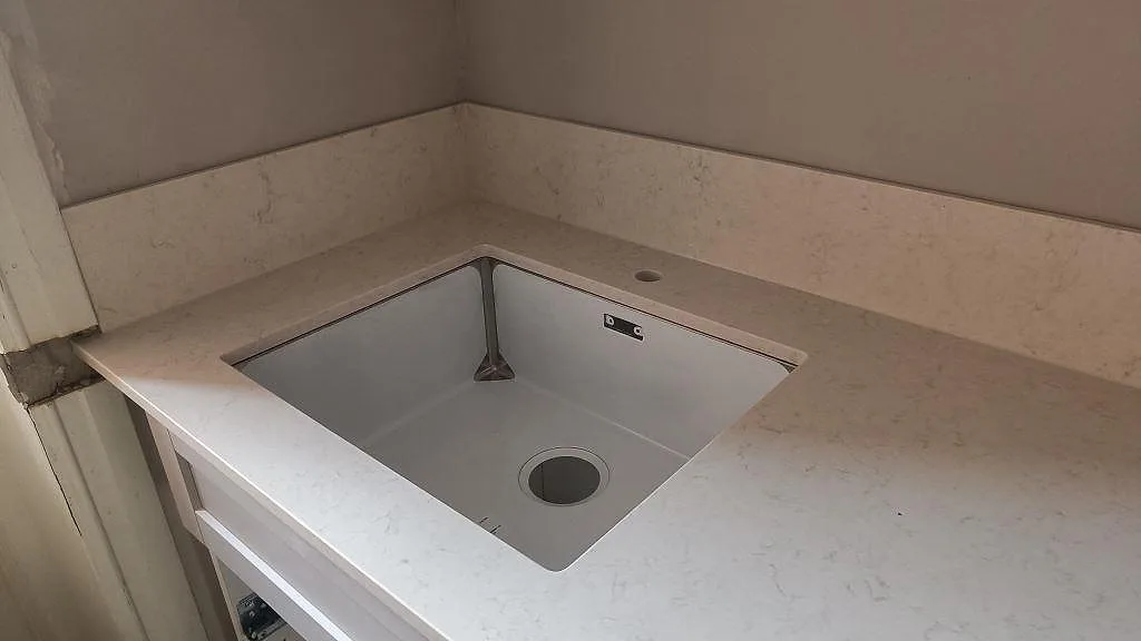 Underlimmad rostfri diskho i en polerad Silestone Snowy Ibiza köksbänkskiva med tappphål och stänkskydd i Malmö.