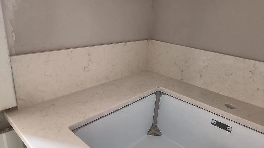 Närbild på rostfri underlimmad diskho och uppvikt stänkskydd i polerad Silestone Snowy Ibiza i ett kök i Malmö.