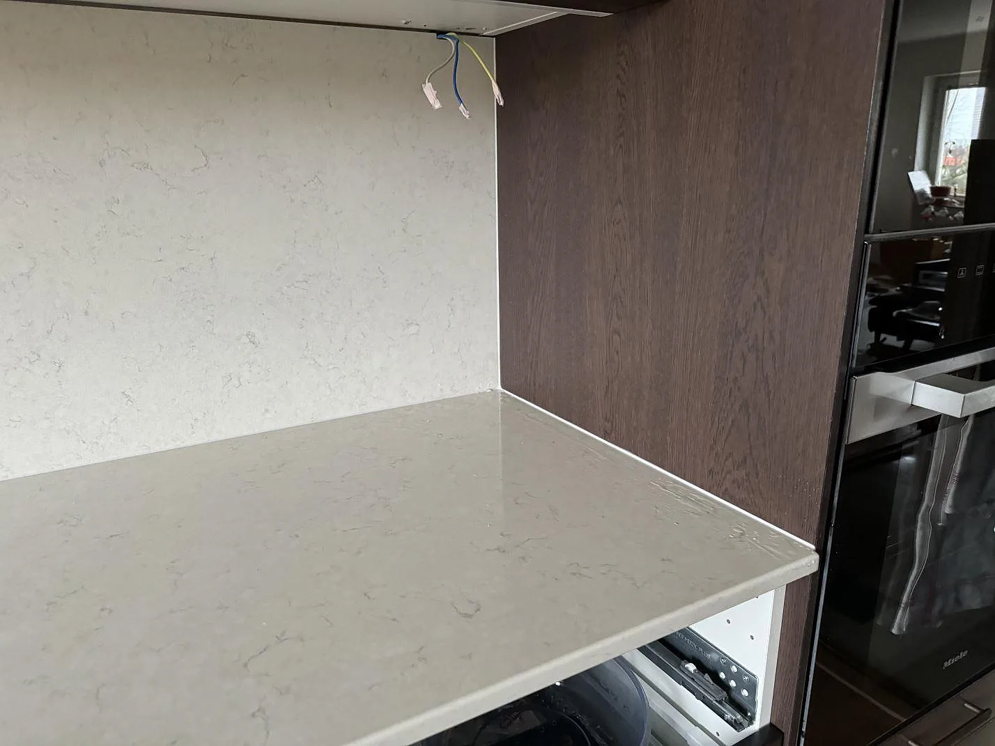 Detalj av ljus köksbänkskiva i polerad Silestone Snowy Ibiza mot mörk träinredning och ugnsskåp i Malmö.