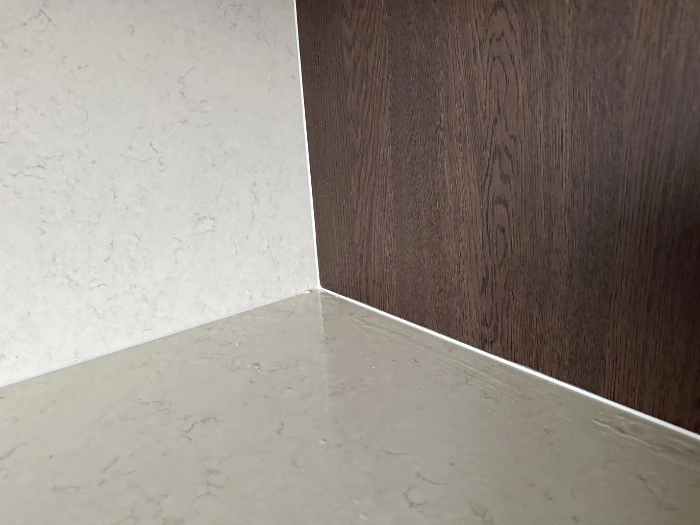 Närbild på mötet mellan polerad Silestone Snowy Ibiza bänkskiva, stänkskydd och mörk träinredning i Malmö.