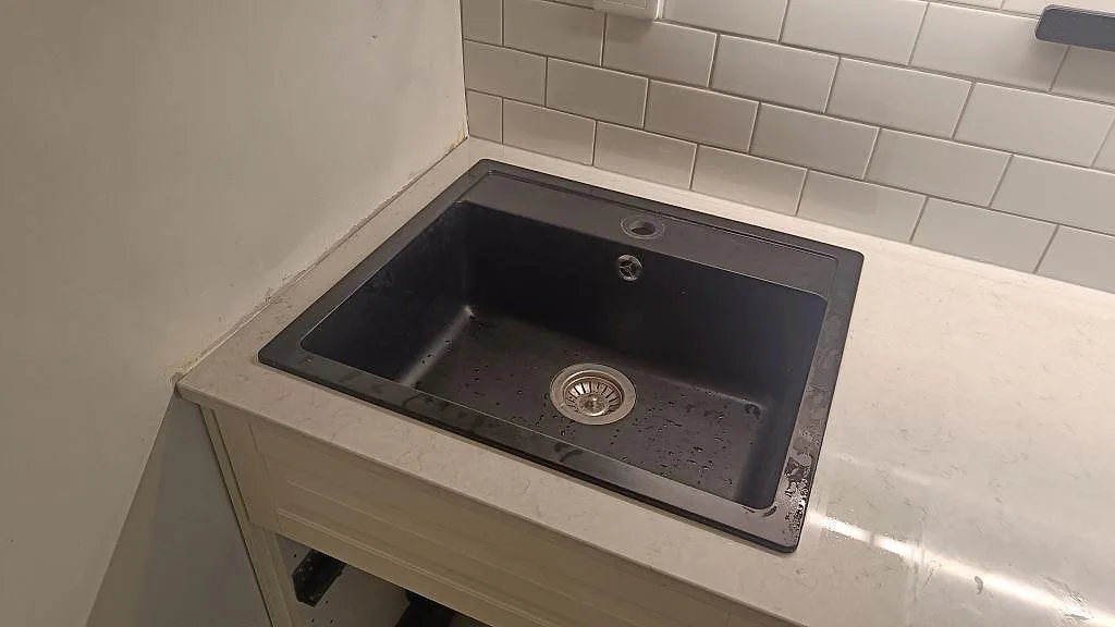 Närbild på polerad Silestone Snowy Ibiza runt en mörk övermonterad diskho med vitt kakel bakom i Malmö.