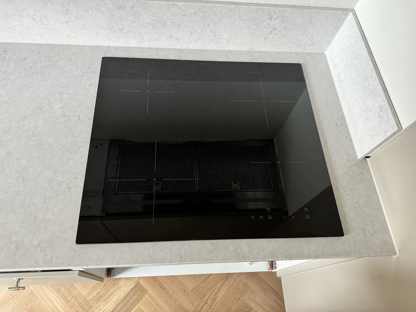 Topvy över svart häll infälld i polerad Silestone Snowy Ibiza, vit kvartskomposit med 12 mm stänkskydd i Malmö.