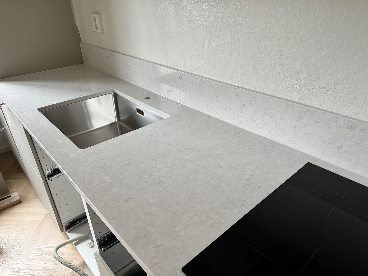 Köksbänkskiva i polerad Silestone Snowy Ibiza, vit kvartskomposit, med underlimmad rostfri diskho, svart häll och stänkskydd i Malmö.