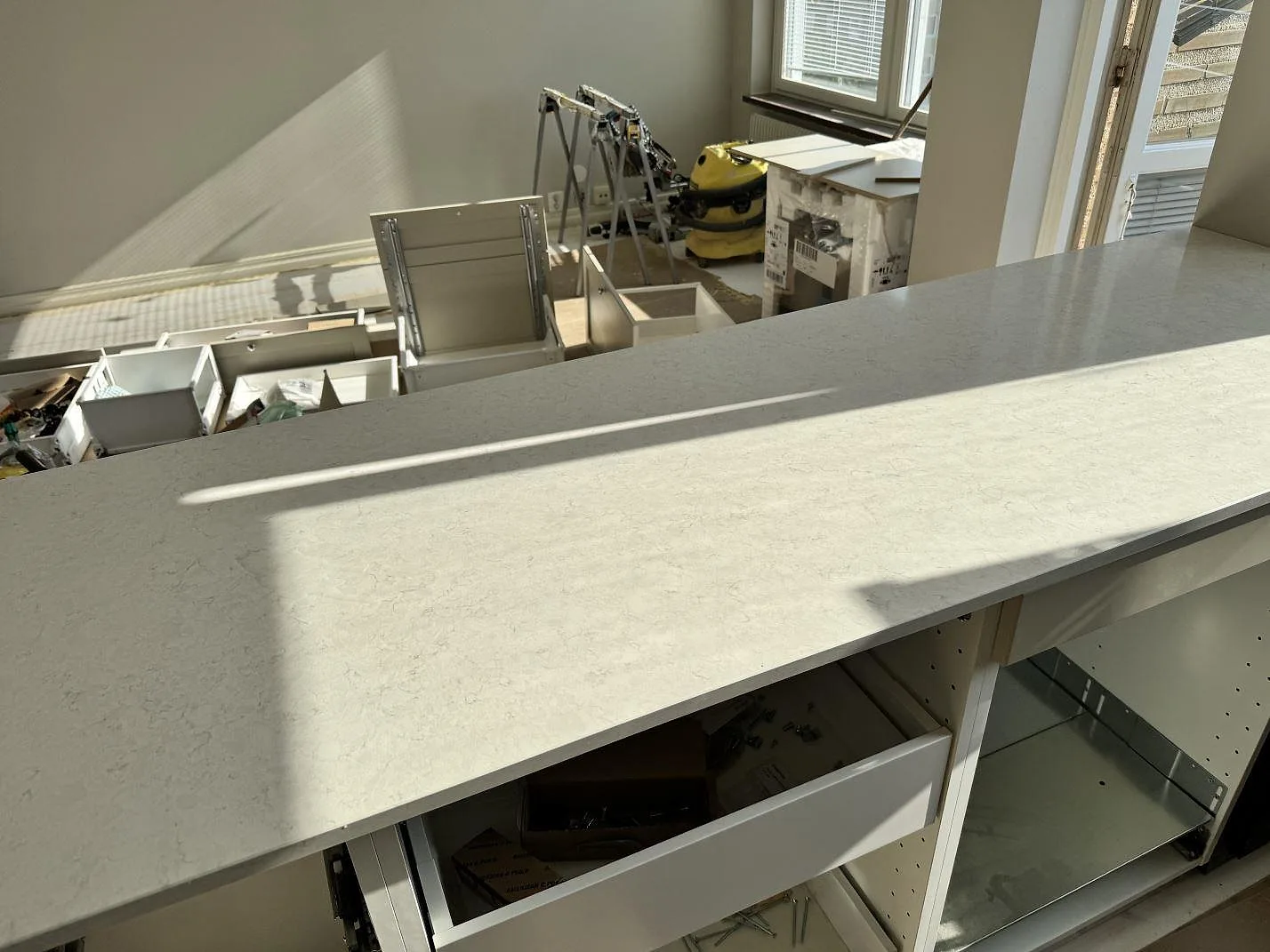 Lång polerad köksbänkskiva i Silestone Snowy Ibiza framför öppna köksstommar i en lägenhetsrenovering i Malmö.