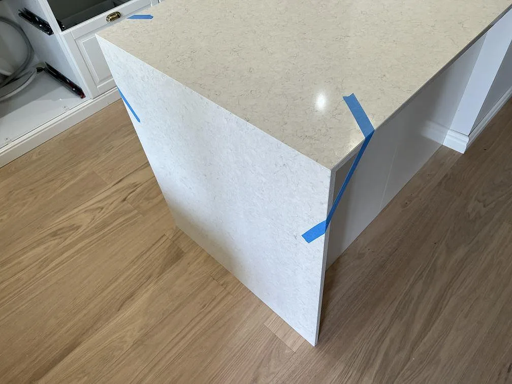 Halvöns gavel i polerad Silestone Snowy Ibiza med tejpade kanter och matchande sten ned mot trägolvet i Malmö.