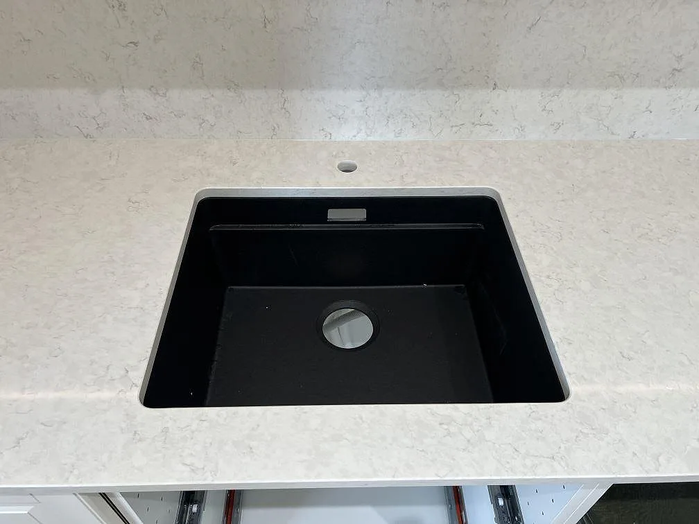 Närbild på underlimmad svart diskho i polerad Silestone Snowy Ibiza med kranhål och matchande stänkskydd i Malmö.